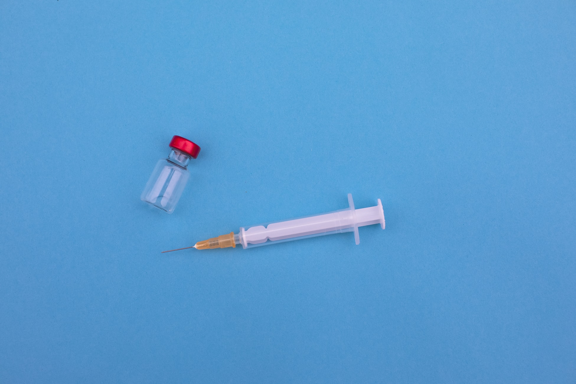 A COVID-19 vaccine vial and syringe rest against a blue background. 